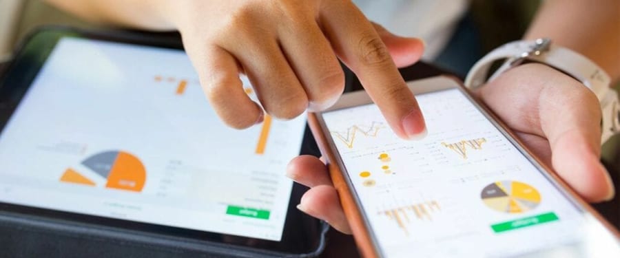 Woman using phone and tablet showing financial graphs